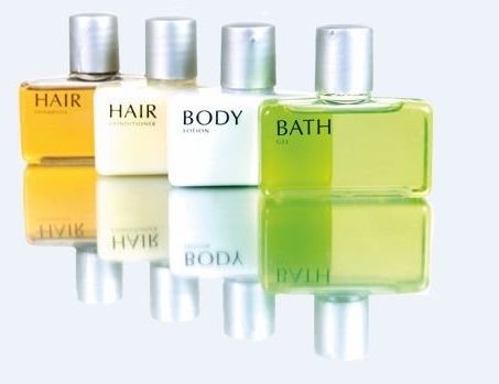 Vier Flaschen mit Pflegeprodukten: Shampoo, Conditioner, Body Lotion und Duschgel, auf einer reflektierenden Oberfläche angeordnet.