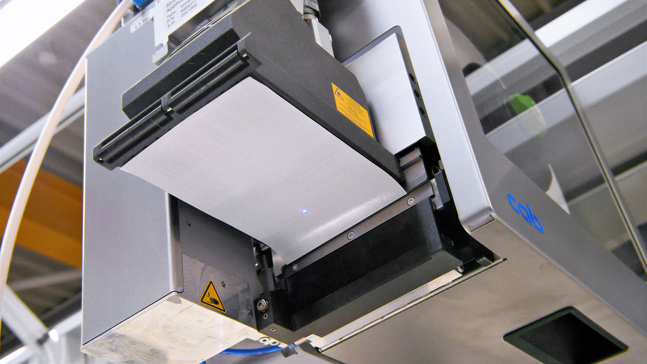 Ein Drucker mit einer leeren Druckeinheit, bereit zum Drucken. Die Maschine zeigt technische Komponenten und Sicherheitskennzeichnungen.
