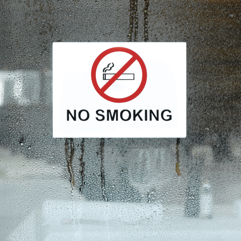 Ein Schild mit der Aufschrift "Rauchen verboten" und einem durchgestrichenen Zigaretten-Symbol, angebracht an einem beschlagenen Fenster.
