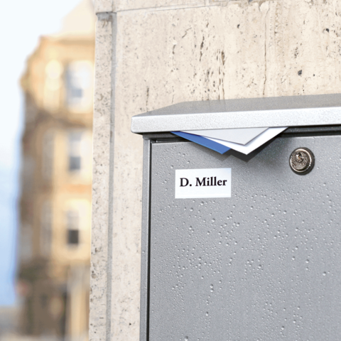 Graue Briefkasten mit dem Namen "D. Miller" auf der Vorderseite, leicht geöffnet und mit Briefen darin.