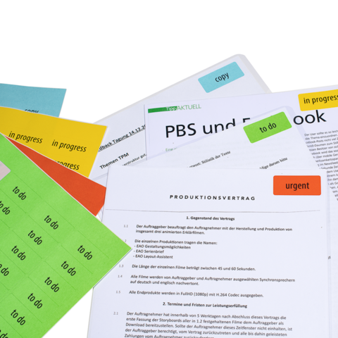 Varios documentos con notas adhesivas de colores, incluyendo un contrato de producción y apuntes sobre PBS y Facebook.