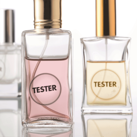 Drei Parfümflaschen, eine mit rosa Flüssigkeit und zwei mit klarer Flüssigkeit, alle mit dem Aufdruck "TESTER".
