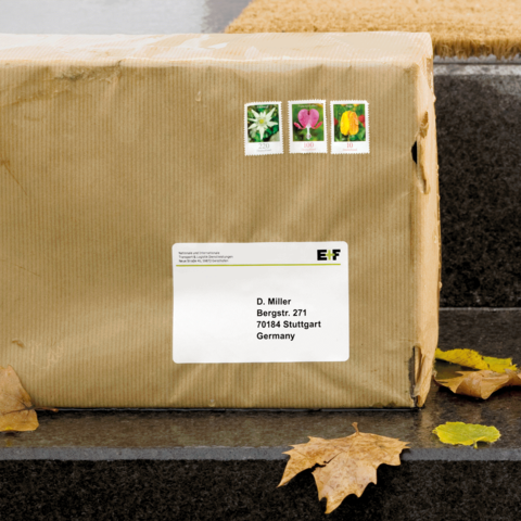 Ein braunes Paket mit drei Briefmarken auf der Oberseite, adressiert an D. Miller in Stuttgart, Deutschland.