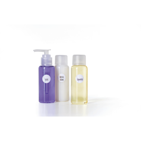 Drei Flaschen mit Pflegeprodukten: eine lila Flasche mit Pumpkopf, eine weiße Flasche und eine gelbe Flasche, beschriftet mit "Shampoo" und "Dusche Creme".