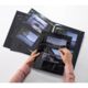 Eine Person blättert durch ein Fotoalbum mit mehreren Bildern von Landschaften und Gewässern.