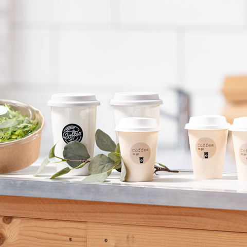 Varios tazas de café están sobre una mesa al lado de un tazón de ensalada. Las tazas tienen pegatinas que indican "Café para llevar".