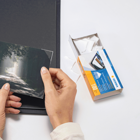 Ein Fotoalbum mit mehreren Bildern, darunter Porträts und Landschaften, sowie einige lose Fotos und eine Packung Fotofilme.