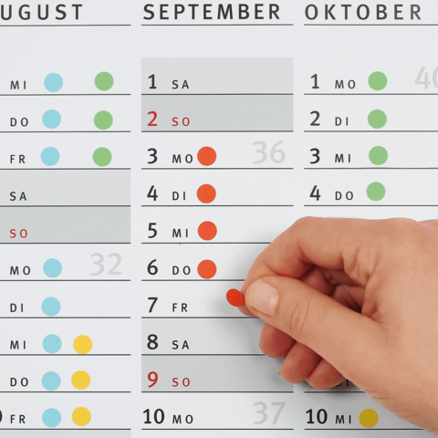 Ein Hand, die einen roten Punkt auf einem Kalender für September und Oktober anzeigt, mit hervorgehobenen Daten.