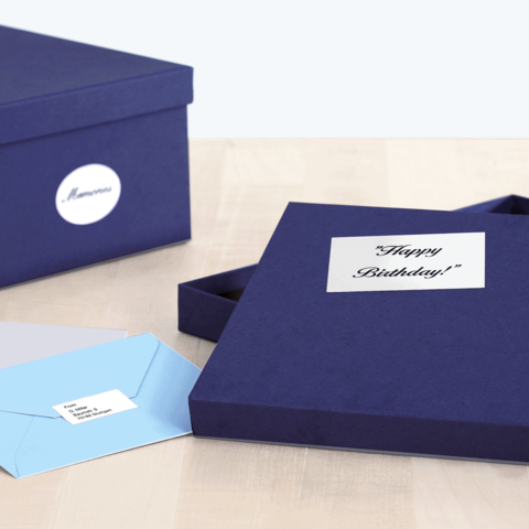Eine geöffnete, dunkelblaue Geschenkbox mit einem "Happy Birthday!"-Aufkleber und zwei Umschlägen in verschiedenen Farben daneben.