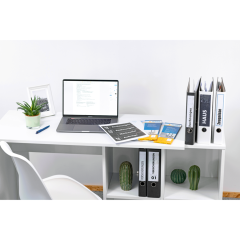 Schreibtisch mit Laptop, Pflanzen und Ordnern. Dokumente liegen auf der Tischoberfläche, darunter sind weitere Ordner auf einem Regal.