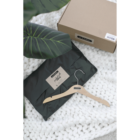 Ein hölzerner Kleiderbügel liegt auf einem weißen Strickteppich neben einer grünen Verpackung und einem Karton.