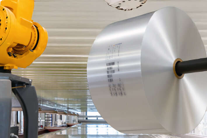 Un brazo robótico industrial amarillo monta un gran componente plateado en un entorno de fabricación moderno.