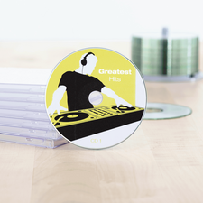 Texto: "CD titulada 'Grandes Éxitos', presentada con un diseño de DJ sobre un fondo amarillo, al lado de una pila de estuches de CD.