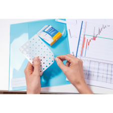 Eine Person hält ein Blatt mit Löchern in der Hand, während sich ein Heftgerät und ein Diagramm auf einem Tisch befinden.