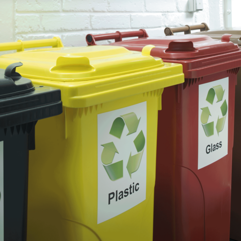 Drei Abfallbehälter in verschiedenen Farben: Gelb für Plastik, Rot für Glas und Schwarz für Restmüll, jeweils mit Recycling-Symbolen.