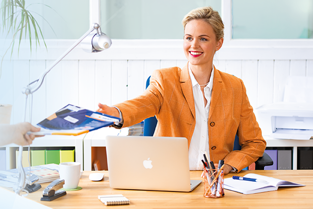 Dos personas en una mesa, presentando etiquetas. A la izquierda, un hombre con hojas de etiquetas; a la derecha, una mujer con una computadora portátil y etiquetas.