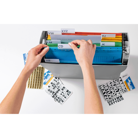 Hände sortieren farbige Akten in einem Ordner mit beschrifteten Trennblättern. Daneben liegen Aufkleber mit Buchstaben.